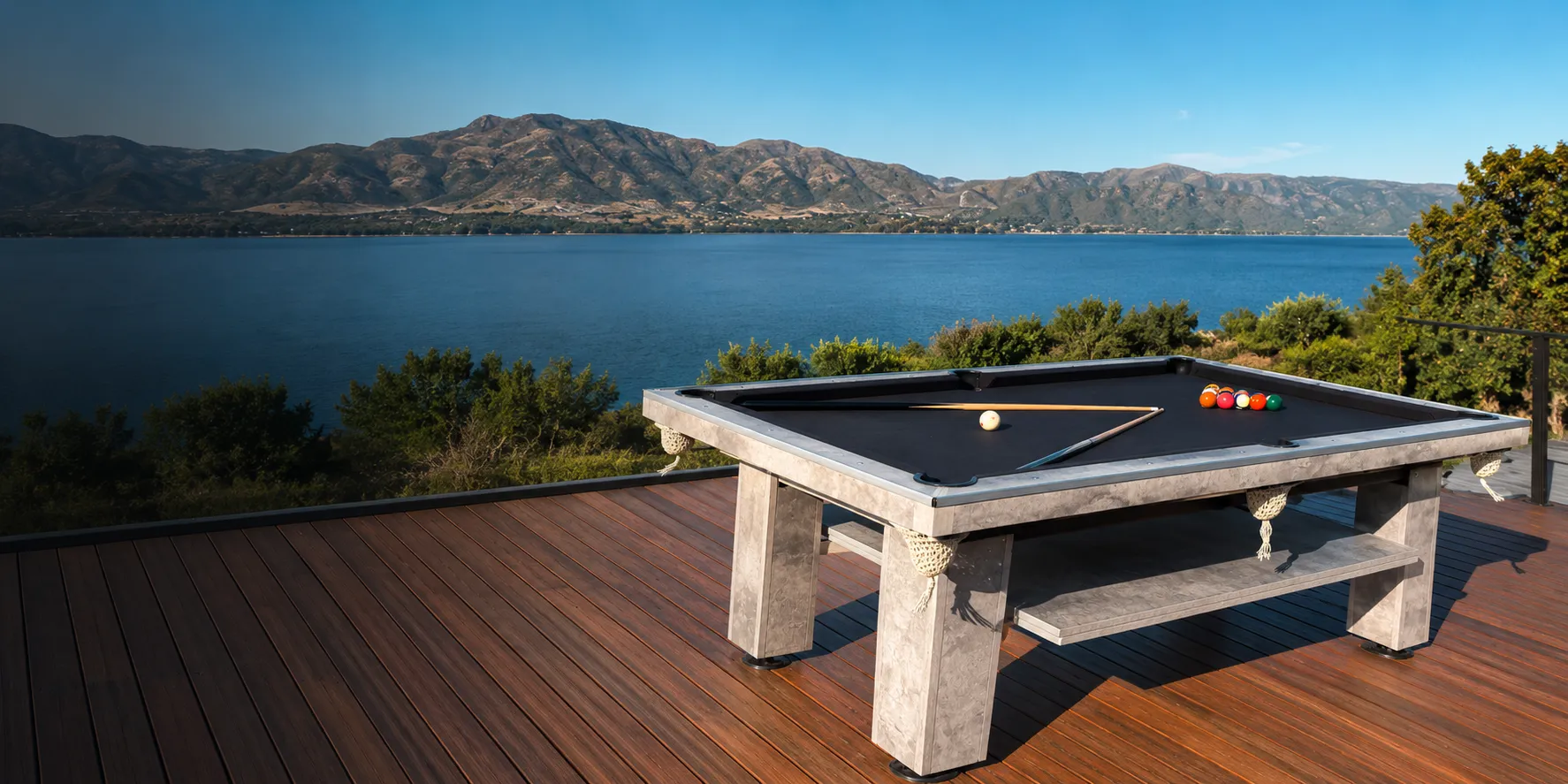 Mesa Black Star Pool de base marmolada gris con paño negro sobre un deck de madera frente a un lago